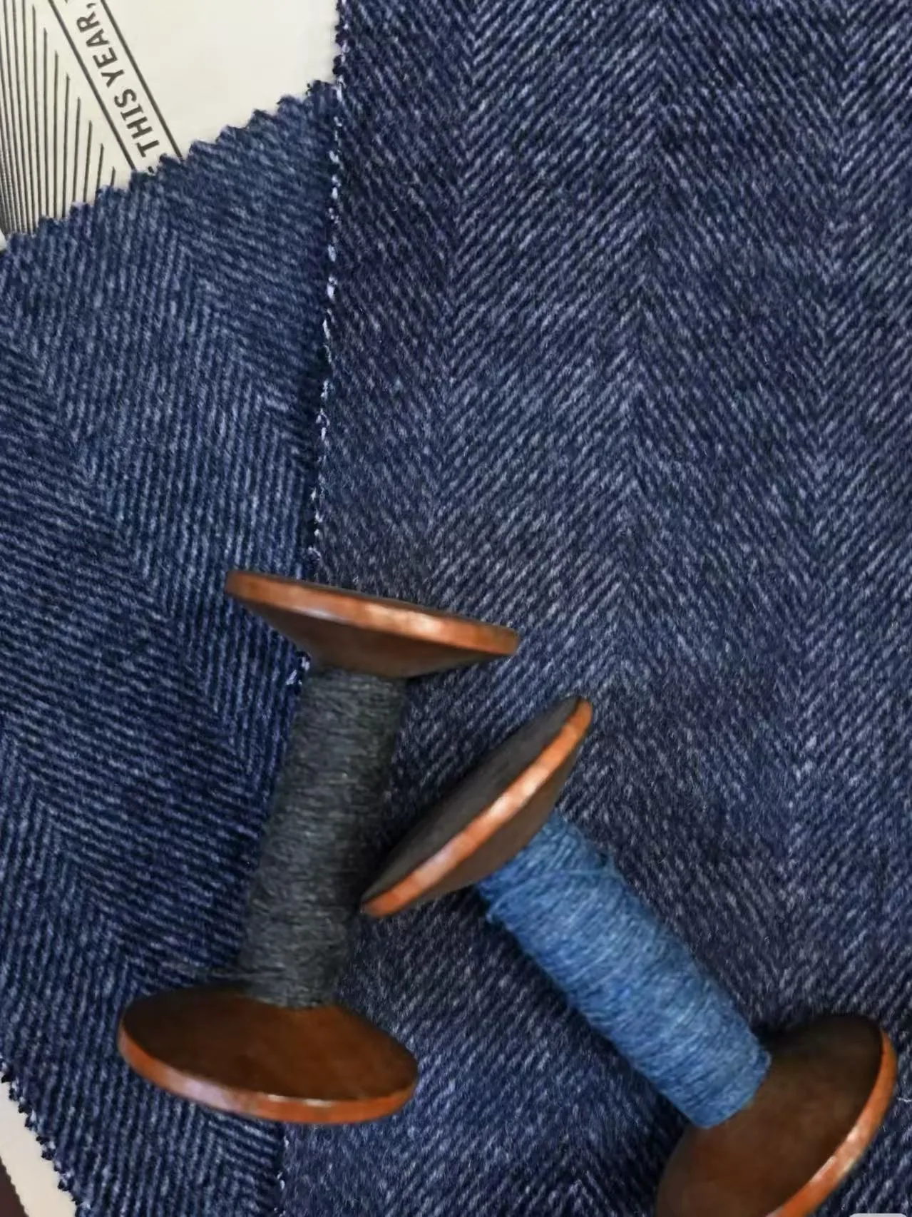 Blue herringbone woolen fabric swatches with matching yarn bobbins